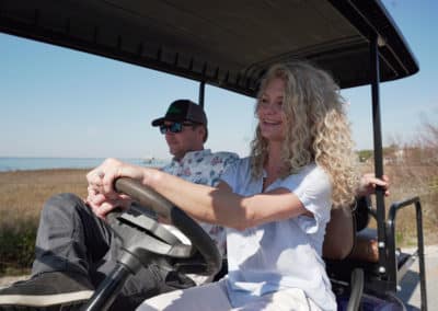 A couple drives a golf cart along a beach, surrounded by sand and ocean, enjoying a sunny day by the shore.