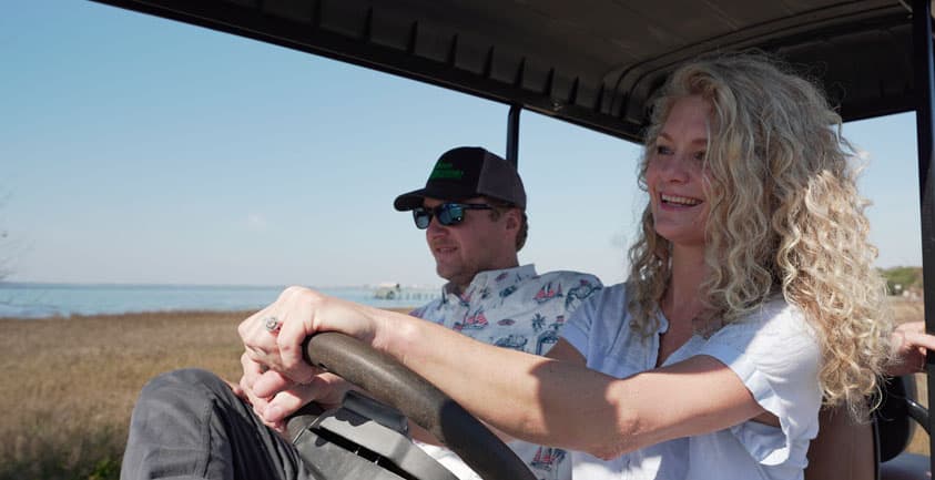 A couple drives a golf cart along a beach, surrounded by sand and ocean, enjoying a sunny day by the shore.