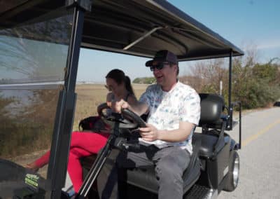 A man and woman driving a low-speed vehicle golf cart along a scenic road.