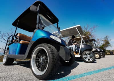 A row of three golf carts parked on a road, representing low-speed vehicles commonly used in golf courses.