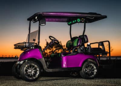 Custom purple golf cart with black and green seats, extra storage, chrome rims, and green led lights